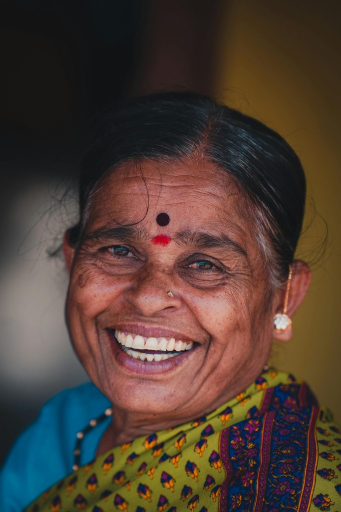 Close-up portrait of a joyful elderly woman wearing a bindi and traditional attire, smiling warmly.